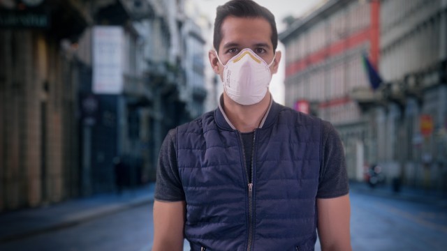 Isolated Man Wearing Protection Face Mask against Coronavirus Covid-19 Standing Still with Empty Streets on the Background. Dramatic impact of Pandemic Virus.