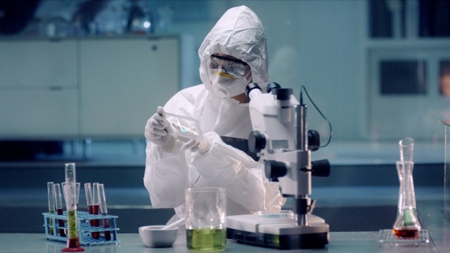 In the Secure High Level Laboratory Scientists in a Coverall Conducting a Research. Chemist analyzes DNA on a digital screen and then Examines It Under Microscope.