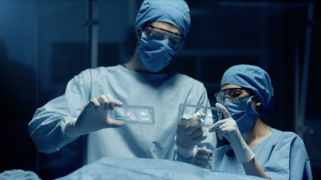 Professional Surgeon and Assistant Analyze Patient Lung Diagnosis Data on Transparent Devices During Surgery. Modern Hospital Operating Room. Shot on RED Epic-W Helium Camera.