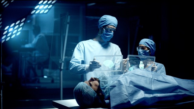 Professional Surgeon and Assistant Analyze Patient Brain Diagnosis Data on Transparent Tablets During Surgery. Modern Hospital Operating Room. Shot on RED Epic-W Helium Camera.