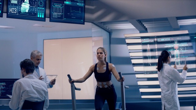 In Science High-Tech Sports Lab Beautiful Athlete Woman walks on treadmill using electrodes attached to her body. Futuristic Screens showing ECG and Medical Data Activity. Shot on Red Epic-W Helium