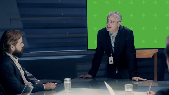 Mockup of Corporate Meeting Room: Executive Director presents data to a Board of Executives about Company’s Future on a Chroma Green Screen Monitor with Trackers. Shot on ARRI ALEXA Mini UHD Camera.