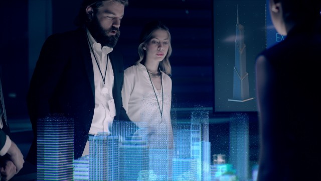In the Near Future: Businessman in Suit presenting Architectural Project to Colleagues and Partners Standing around Futuristic Table with Holographic Modern Augmented Reality Technology.