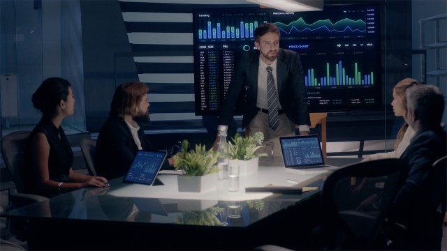 Corporate Meeting Room: Professional Male Executive presents Company Positive Results to Clients and Partners  on a large Monitor with Graphs and Charts. Shot on ARRI ALEXA Mini UHD Camera.